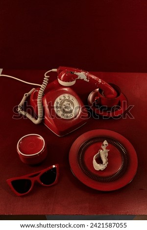 Retro-themed still life with red phone, sunglasses, pearls, and magazine on crimson background