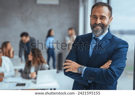 Confident businessman posing in the office, he is smiling at camera. Portrait of happy mature businessman looking at camera. Multiethnic satisfied man with beard feeling confident at office. 