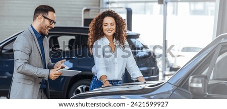 Woman in the showroom enjoying luxury car. Happy salesman selling the car to his female customer in a showroom. Auto business, car sale, consumerism and people concept