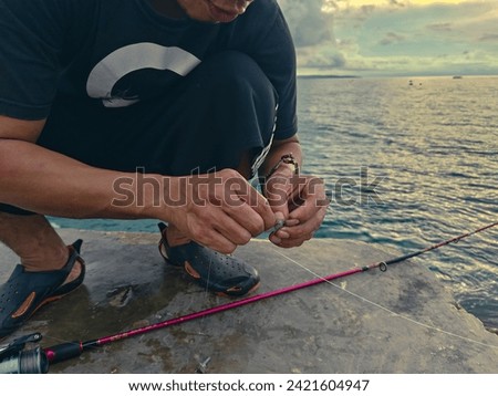 An unidentified individual enjoys a moment of solitude while preparing his fishing line against a backdrop of a mesmerizing sunset over Indonesia’s calm seas.