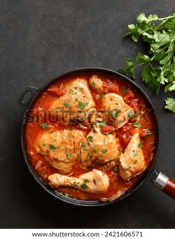 Georgian chicken stew with tomatoes and herbs (chakhokhbili) in cast iron skillet over dark stone background. Baked chicken with tomato vegetable gravy. Top view, flat lay Royalty-Free Stock Photo #2421606571