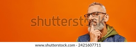 focused mature man in green hoodie with glasses and gray beard posing on orange background, banner