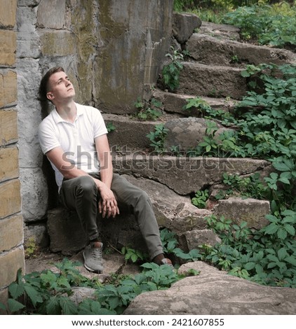 Young teen age mental fail despair grief boy feel hope travel seat retro vintag town brick ruin bush text space Tired lost human guy wait cry worship God believ old rustic village hill home house wall Royalty-Free Stock Photo #2421607855