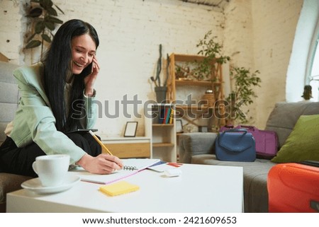 Young happy woman talking on mobile phone with travel agent, hotel and booking her trip, making notes, preferences about tours. Concept of traveling, online services for booking, tourism, vacation
