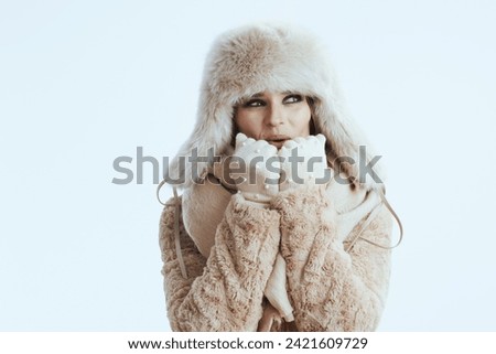 smiling modern woman in winter coat and fur hat isolated on white in white gloves warming hands with breath.