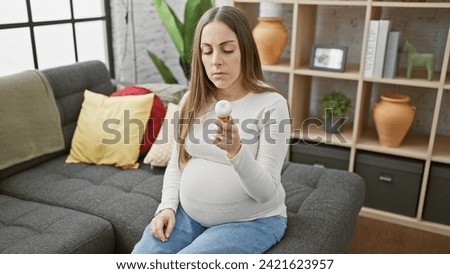 Pregnant hispanic woman examines prescription bottle in a cozy living room setting, symbolizing health and prenatal care.