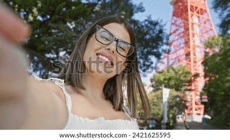 Beautiful hispanic woman in glasses, enjoying her tokyo travel adventure, takes cheery selfie at famous tokyo tower spot