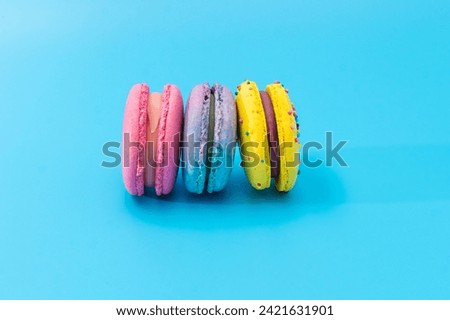 Brightly colored stacked macarons on blue background. Tasty colorful macaroon assorted. Three sweet macaroons cakes of different colors. Delicious dessert. Culinary, cooking concept.