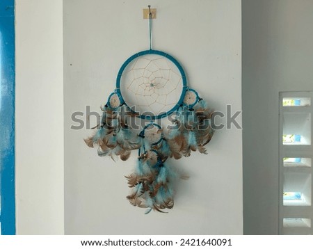 Turquoise blue dream catcher wall decoration on the wall.  Dream catchers are made from threads woven like a spider's web and decorated with feathers.  Negative space selective focus.
