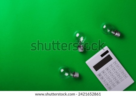 incandescent lamp with white calculator on green background.  Energy efficiency concept. Flat lay. Concept ecology, save planet earth, idea, save energy, economy, saving. Earth day.
