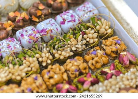Close-up of an assortment of fine, sweet petits fours, beautifully decorated with gold leaf, pine nuts and dried fruit. Royalty-Free Stock Photo #2421655269