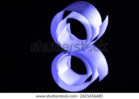A macro closeup image of a strip of paper curled into a spiral.  Lit with a side on blue light and set against a black background, the paper is reflected in a mirror.