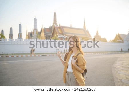 Traveler asian woman 30s, backpack slung over her shoulder, explores the intricate details of Wat Pra Kaew with childlike wonder. Sunlight dances on the golden rooftops.