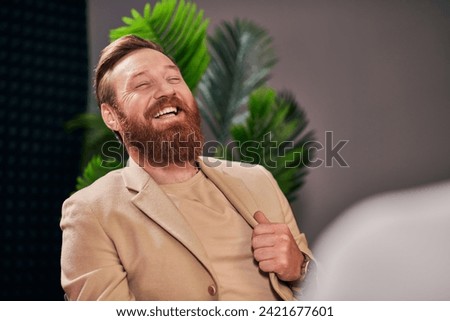 handsome cheerful man with beard in elegant attire laughing during interview while in studio