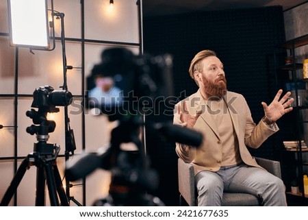 handsome man with red hair and beard in elegant outfit talking actively during podcast in studio
