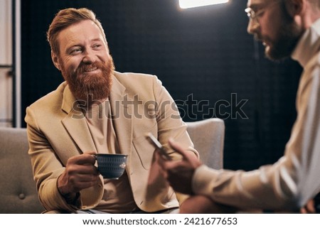 jolly red haired man talking to his interviewer in glasses that holding smartphone during discussion