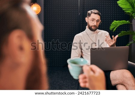 handsome chic men in elegant attires with coffee and laptop discussing interview questions Royalty-Free Stock Photo #2421677723