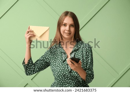 Pretty young woman with mobile phone and envelope on green background