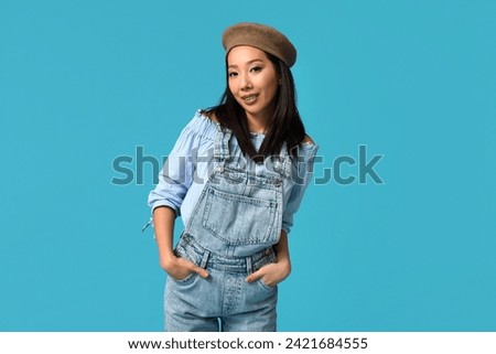 Beautiful young happy Asian woman in stylish denim jumpsuit on blue background Royalty-Free Stock Photo #2421684555
