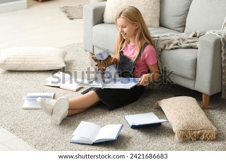 Cute little girl reading book while sitting on floor at home