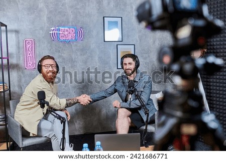 handsome interviewer and his guest in casual attires shaking hands and smiling happily, podcast