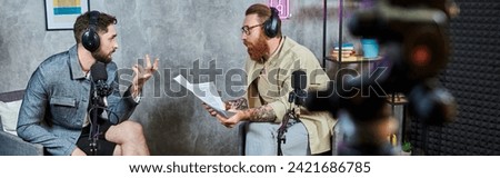 two handsome bearded men in casual attires with headphones talking actively during podcast, banner