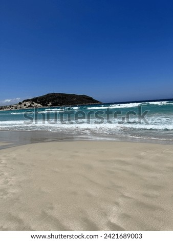 The image showcases a tranquil beach with clear blue skies, turquoise waters, and unspoiled white sands leading to a hilly island in the distance. Royalty-Free Stock Photo #2421689003