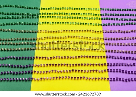 Colorful beads for Mardi Gras celebration on color background