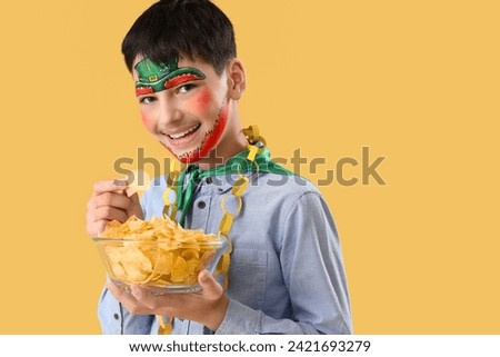 Funny boy with face painting and potato chips on yellow background. St. Patrick's Day celebration