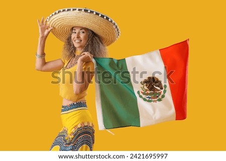 Mature woman in sombrero hat with flag on yellow background. Mexico's Day of the Dead (El Dia de Muertos) celebration Royalty-Free Stock Photo #2421695997