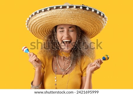 Mature woman in sombrero hat with maracas on yellow background. Mexico's Day of the Dead (El Dia de Muertos) celebration Royalty-Free Stock Photo #2421695999