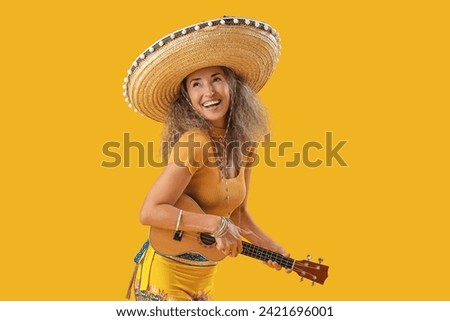 Mature woman in sombrero hat playing guitar on yellow background. Mexico's Day of the Dead (El Dia de Muertos) celebration Royalty-Free Stock Photo #2421696001