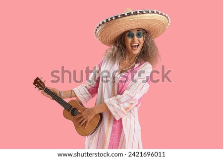 Mature woman in sombrero hat playing guitar on pink background. Mexico's Day of the Dead (El Dia de Muertos) celebration Royalty-Free Stock Photo #2421696011
