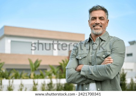 Happy mature older Latin man new property buyer modern villa owner or realtor salesman standing outside home, smiling middle aged homeowner posing outdoor near country house. Portrait. Royalty-Free Stock Photo #2421700341