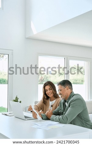 Happy mature couple calculating money expenses savings using laptop at home. Middle aged man and woman checking receipts for tax refund, paying bills online sitting at table in living room. Vertical. Royalty-Free Stock Photo #2421700345