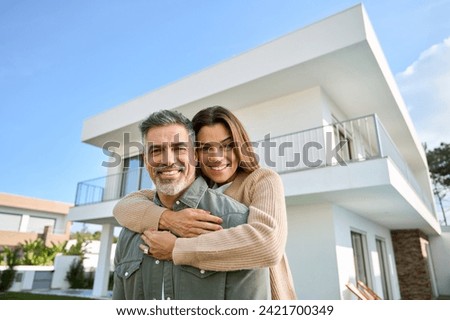 Happy smiling mature older family couple new property buyers modern dream luxury villa owners standing outside house, affectionate senior middle aged man and woman in love hugging outdoor. Portrait.