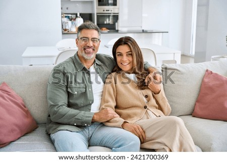 Happy smiling healthy middle aged romantic couple mature man and woman hugging sitting on sofa at home together relaxing on couch looking at camera in modern house living room. Portrait. Royalty-Free Stock Photo #2421700369