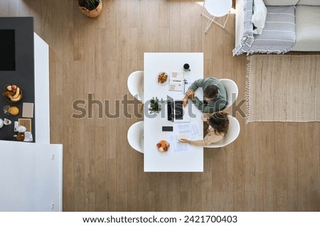 Middle aged man and woman using laptop computer sitting at table in living room interior. Mature couple calculating finance expenses, money savings, paying bills online at home. Top view from above. Royalty-Free Stock Photo #2421700403