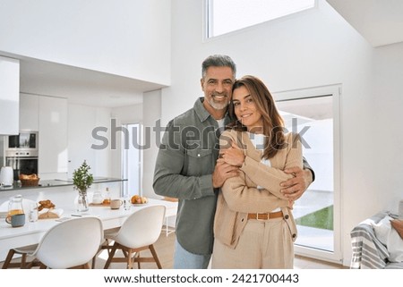 Happy smiling middle aged romantic affectionate couple mature older man and woman hugging standing at home together looking at camera enjoying bonding in modern house living room. Portrait. Royalty-Free Stock Photo #2421700443