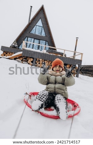 Portrait of a happy child riding a sled and enjoying a winter active vacation. Snowy winter entertainment. 