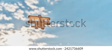 Wooden, made of plywood, small toy light aircraft biplane with propeller, flying in cloudy sky, illuminated by sunlight. Cartoon. Copy space. Banner