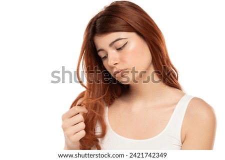 Worried redhead woman inspecting her hair ends on a white studio background Royalty-Free Stock Photo #2421742349