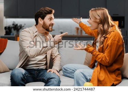 Portrait of angry unhappy couple, man and woman quarreling, shouting loudly sitting on sofa at home, gesturing. Concept of abusive relationships