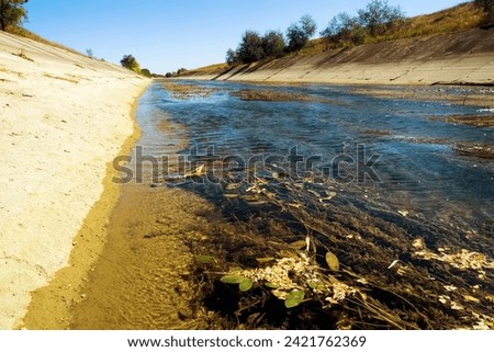 Concrete water conducting channel, irrigation canal became shallow, silting (obliteration) and overgrown with aquatic plants (macrophytes) due to lack of water and current now Royalty-Free Stock Photo #2421762369