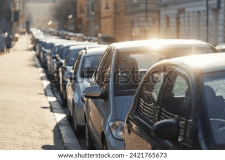 Scenic sunlit view row parked cars on busy city street in european city. Sidewalk parallel side parking full of vehicles traffic jam in downtown on warm sunset evening or sunrise morning Royalty-Free Stock Photo #2421765673