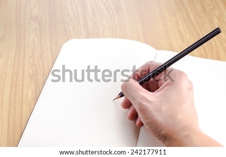 Hand holding black pencil writting on blank open notebook on wood table,business template.