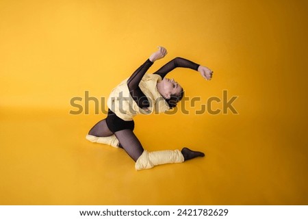 Portrait of a young girl in a yellow down jacket and a black bodysuit dancing on a yellow background. Sporty way of life, style, interesting stylish look. Concept of sport, hobby, fitness, fashion.