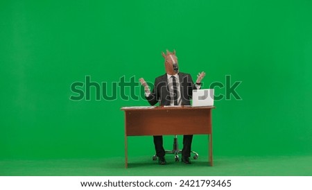 Man in business suit with horse head mask on studio green background. Businessman sits at desk, says something and points his hand to the sides. Concept of heavy office work. Royalty-Free Stock Photo #2421793465