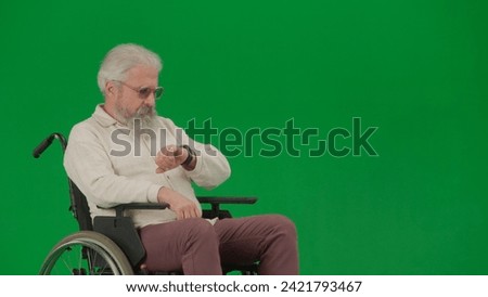 Portrait of aged man on chroma key green screen background. Elderly man sitting in a wheelchair and looking at the clock.