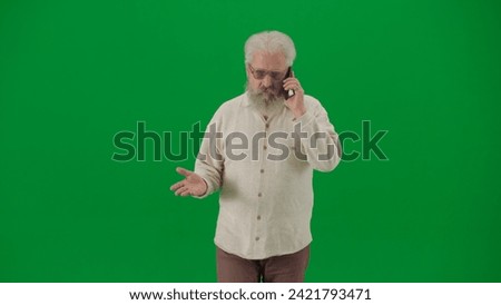 Portrait of aged bearded man on chroma key green screen. Senior man walking and looking at the camera, talks on smartphone
